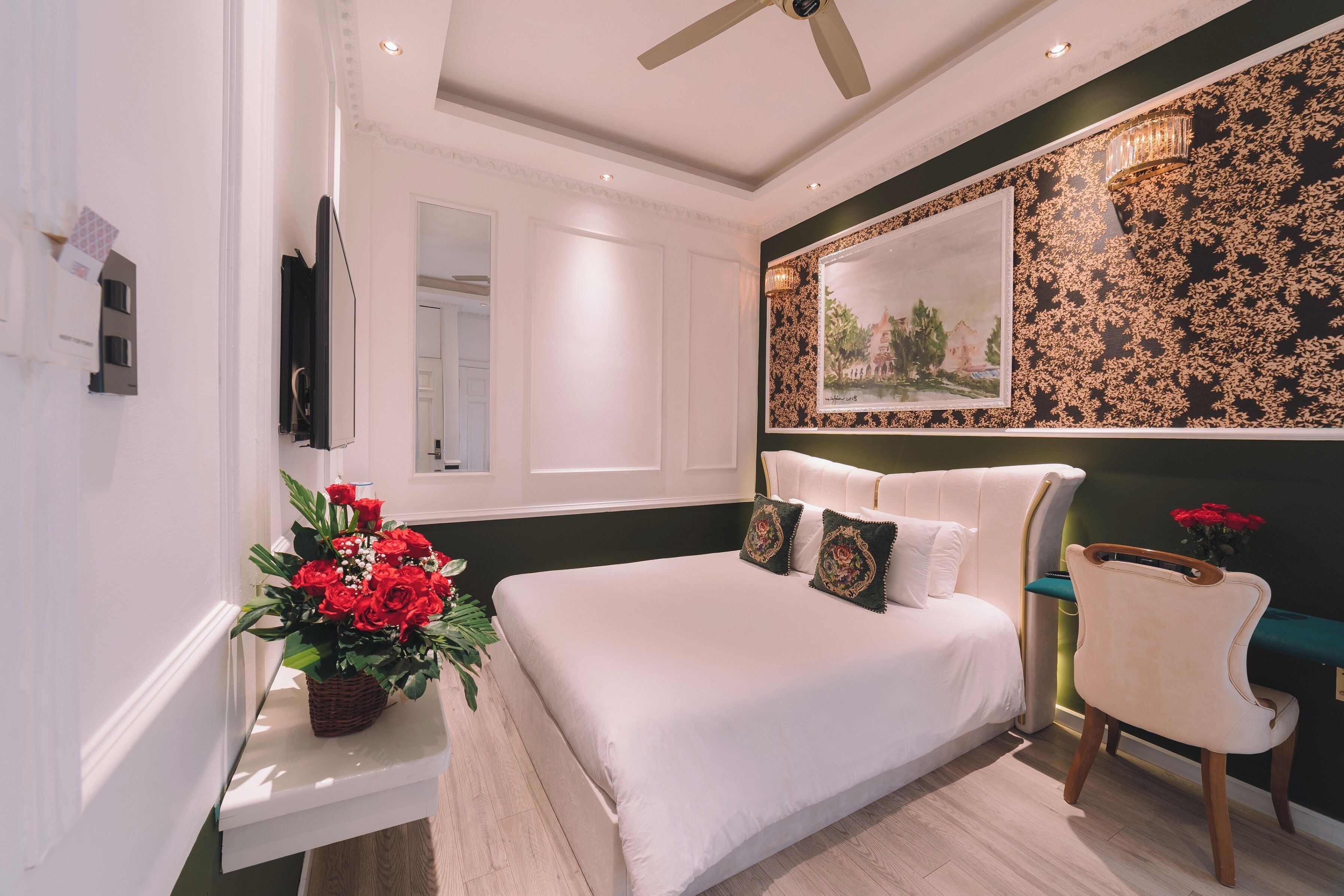 A bedroom with a large bed, a chair, a painting on the wall, and a ceiling fan.