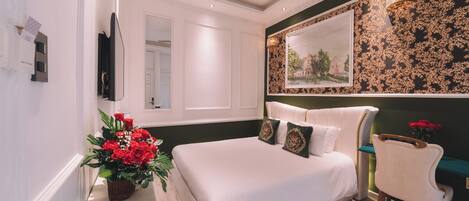 A bedroom with a large bed, a chair, a painting on the wall, and a ceiling fan.