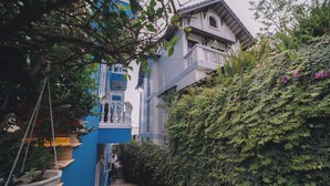 Un estrecho callejón con pavimento a rayas de colores, un edificio azul con balcón y una pared cubierta de vegetación.