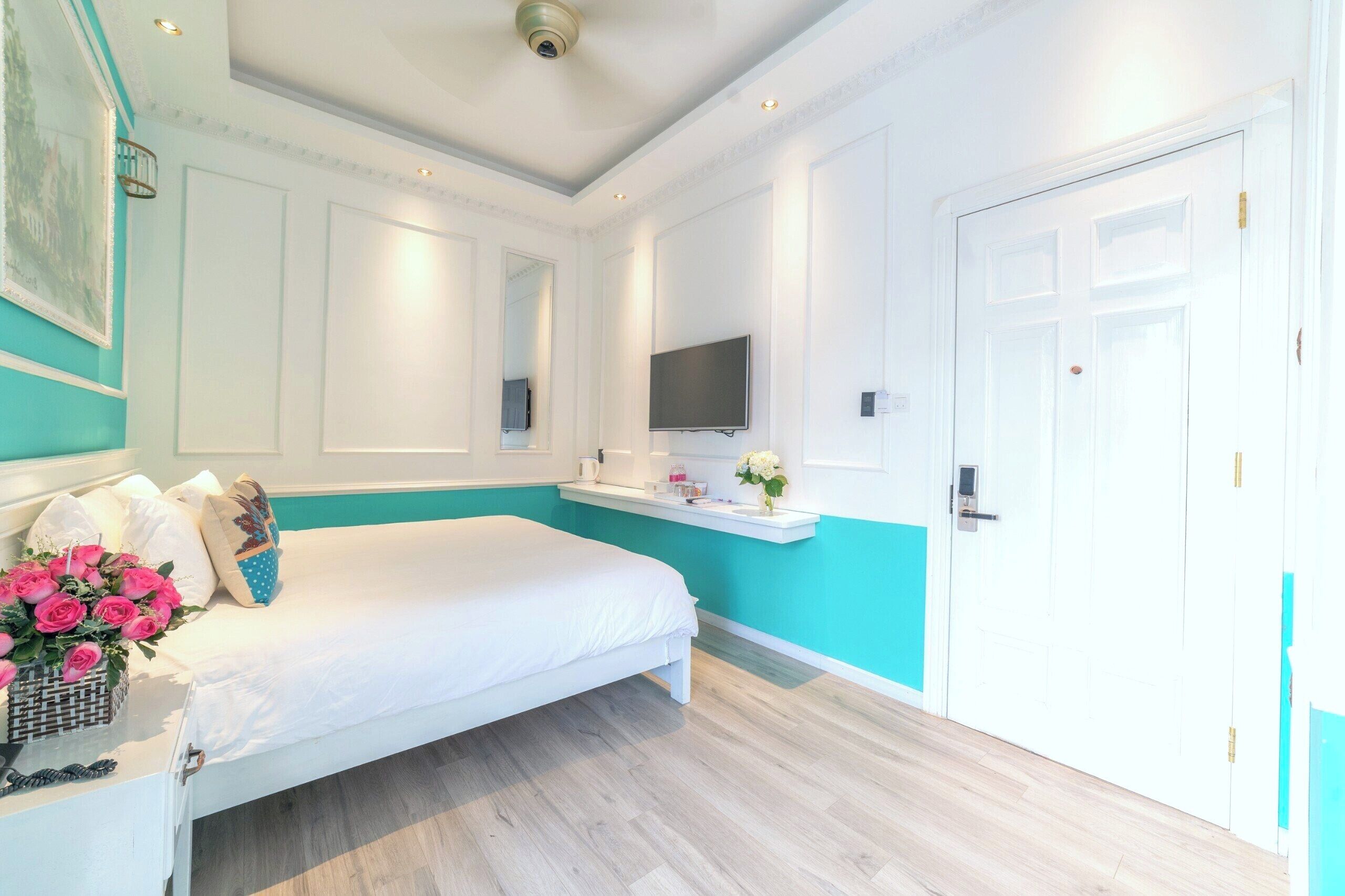 Un dormitorio con una cama, un televisor, una puerta blanca y un estante con un jarrón de flores.