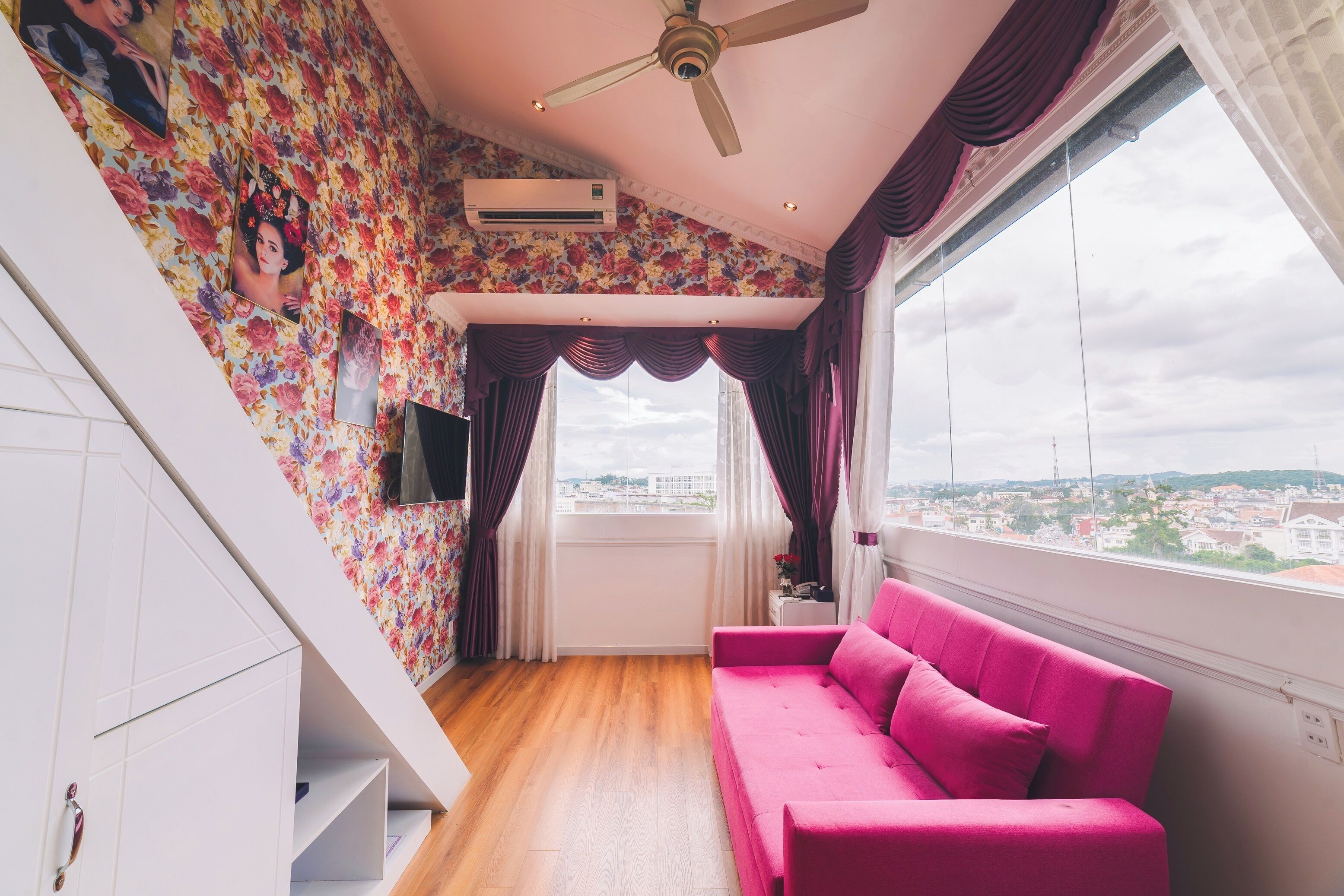 Ein Zimmer mit einem rosafarbenen Sofa, einer Treppe mit floralem Wandpapier und Blick auf die Stadt durch das Fenster.
