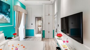 Una habitación de hotel con una cama grande, un televisor, un baño con cortina de ducha estampada y paredes color turquesa.
