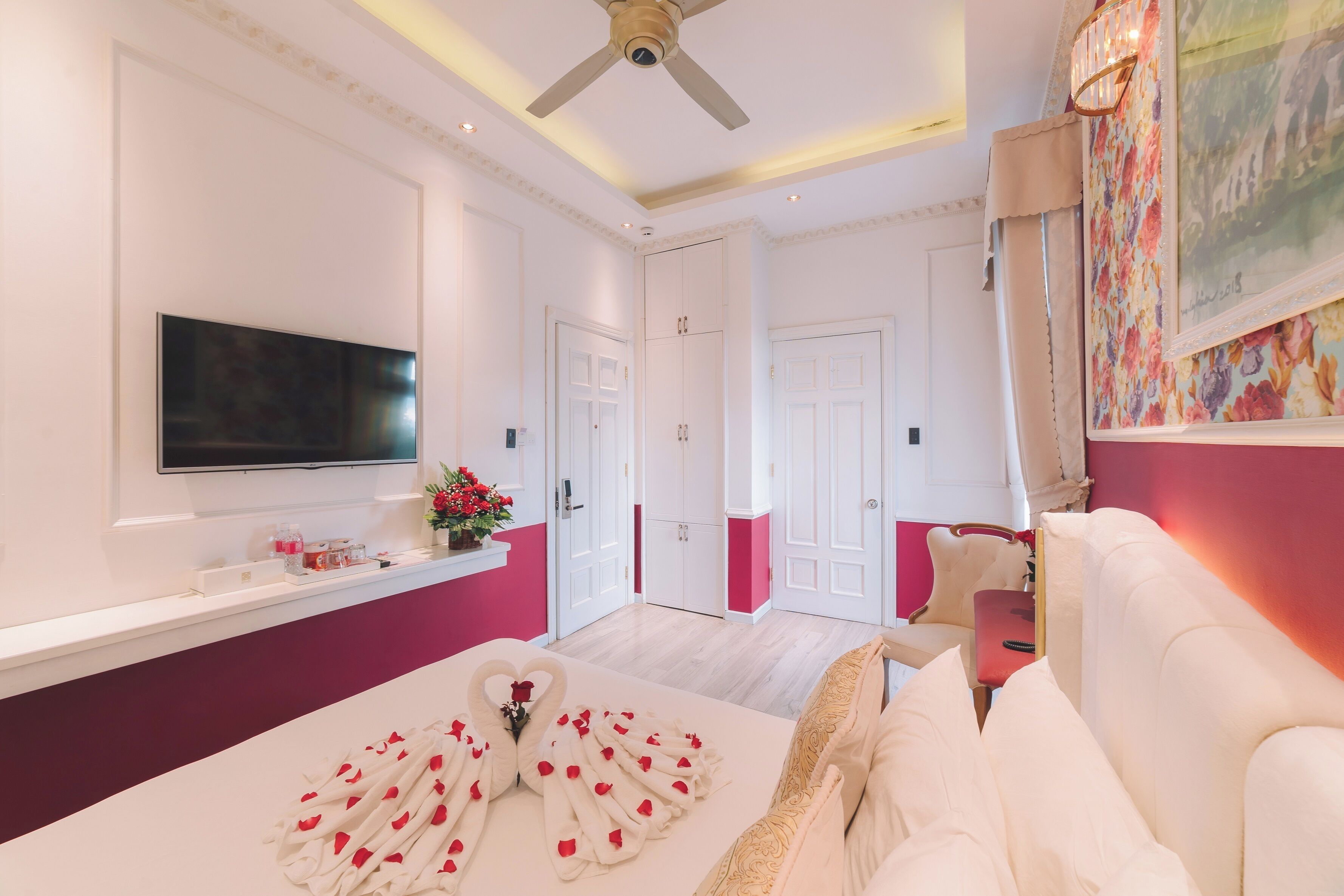 Una habitación de hotel con cama, televisión, ventilador de techo y puerta que da a otra habitación.