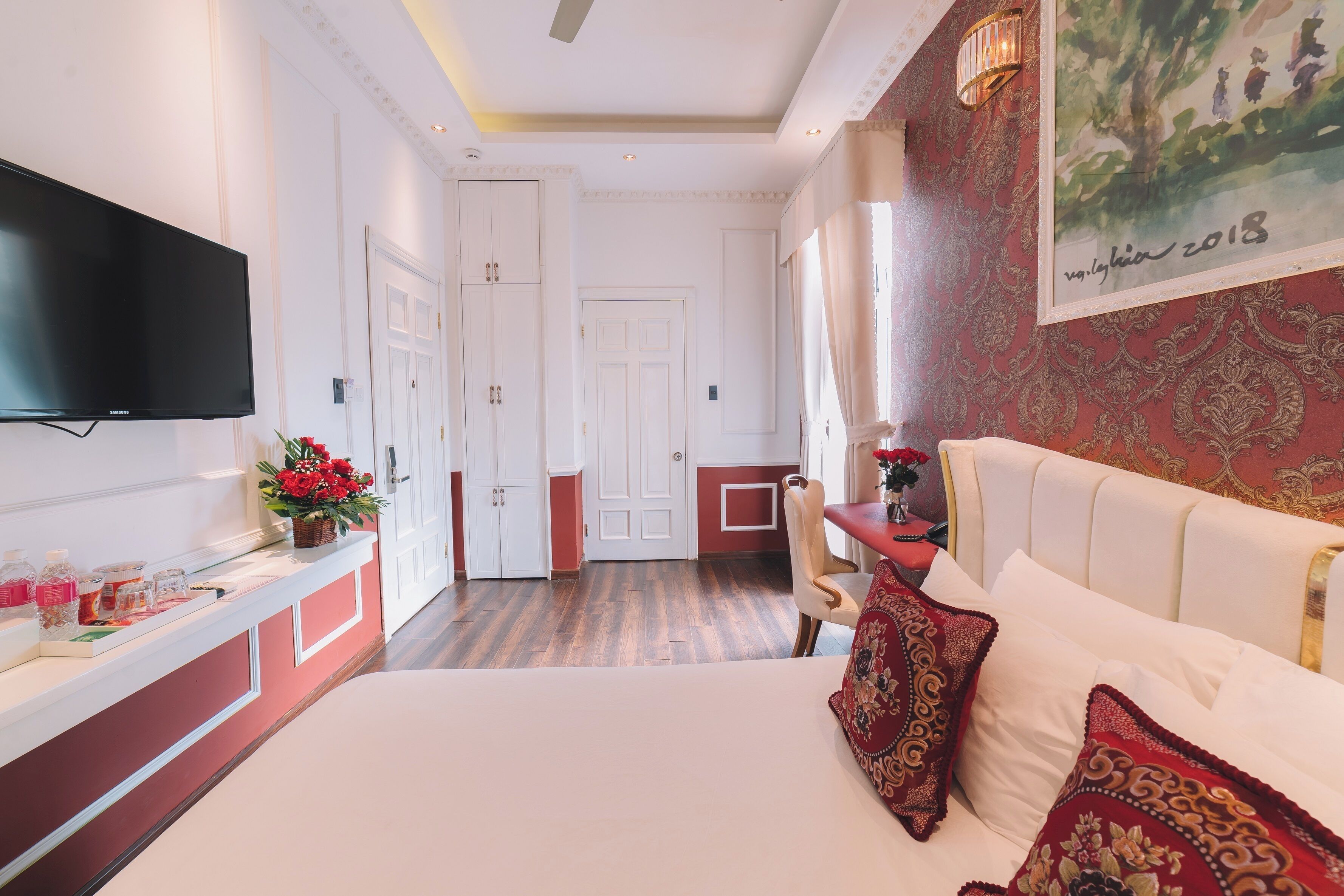A hotel room with a bed, a TV, a desk, and a chair. There is a door leading to another room.
