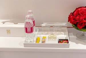 Una bandeja con una botella de agua, una caja de pañuelos, un objeto amarillo pequeño, un objeto rojo y una tarjeta sobre una superficie blanca.