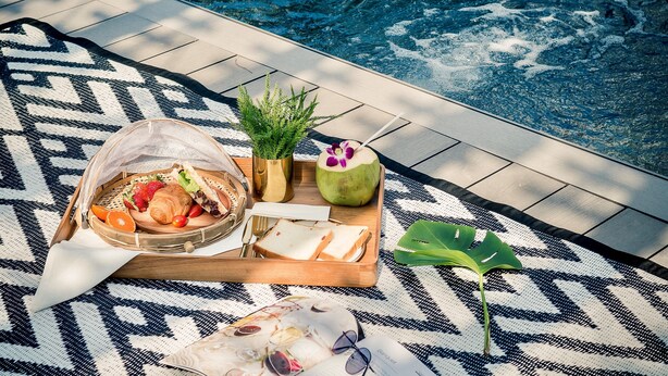Disposición junto a la piscina con una bandeja de comida, una bebida y una planta.
