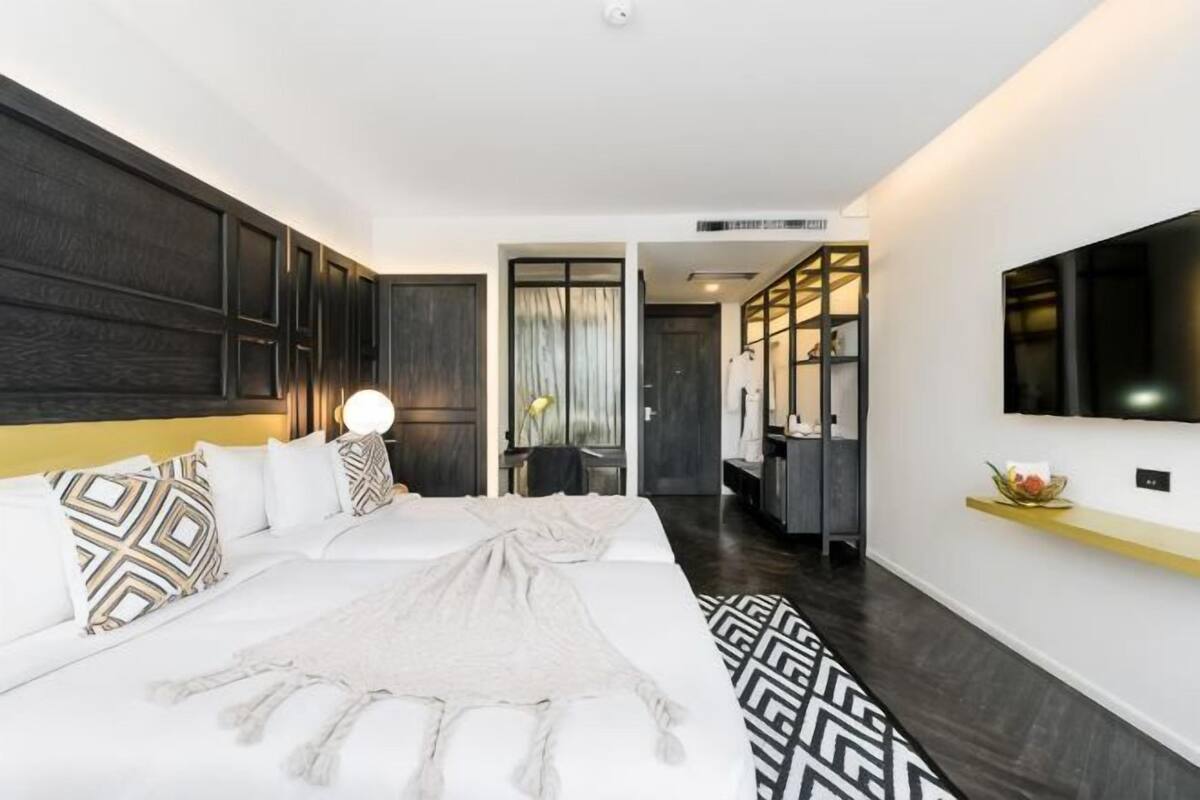 A modern hotel room with a large bed, a TV, and a hallway leading to a bathroom.