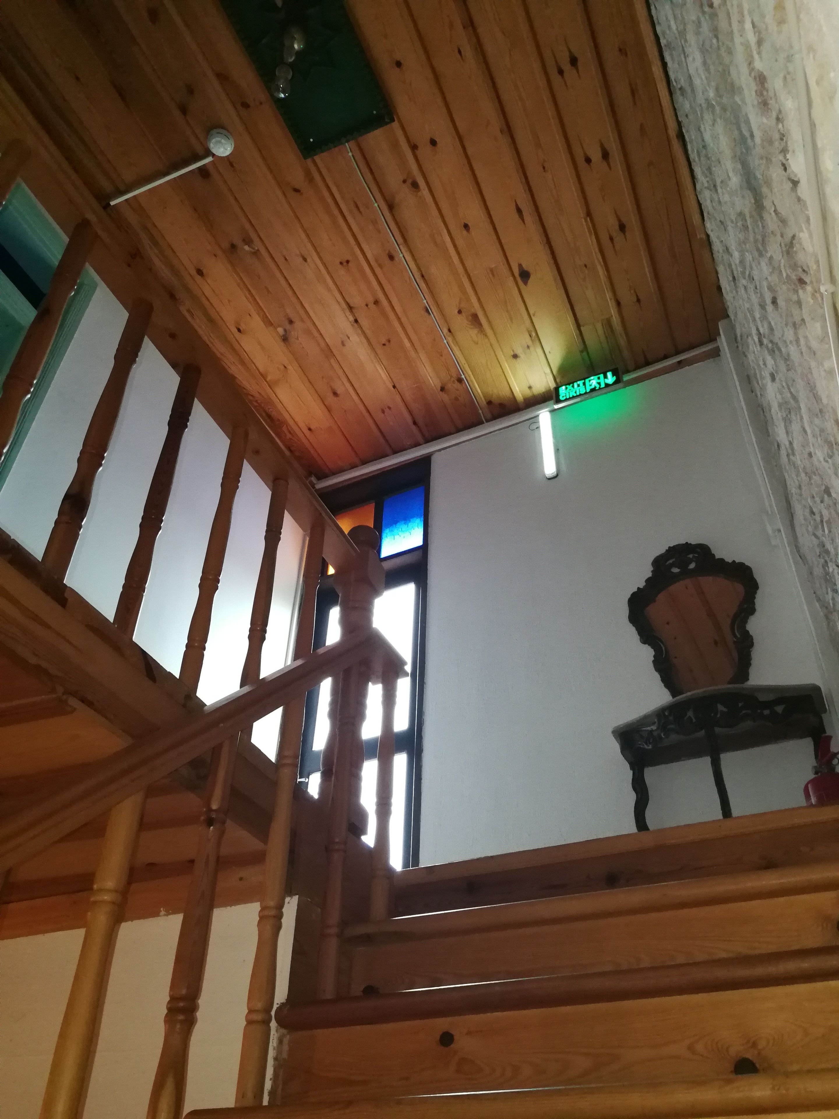 A wooden staircase with a handrail, a wall-mounted light fixture, and a window with a view of the outside.
