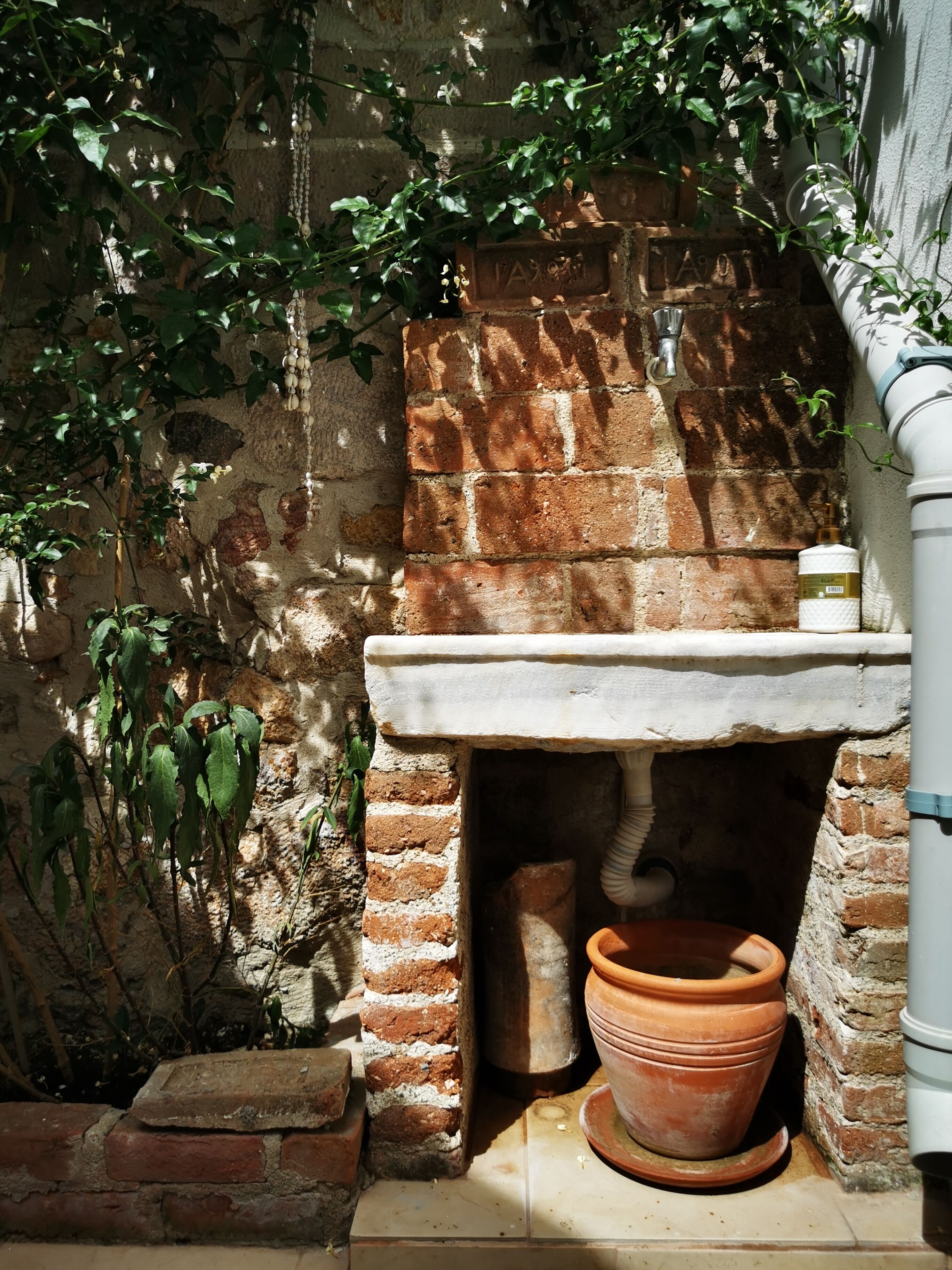 A rustic outdoor bathroom with a brick wall, a stone sink, and a terracotta pot.