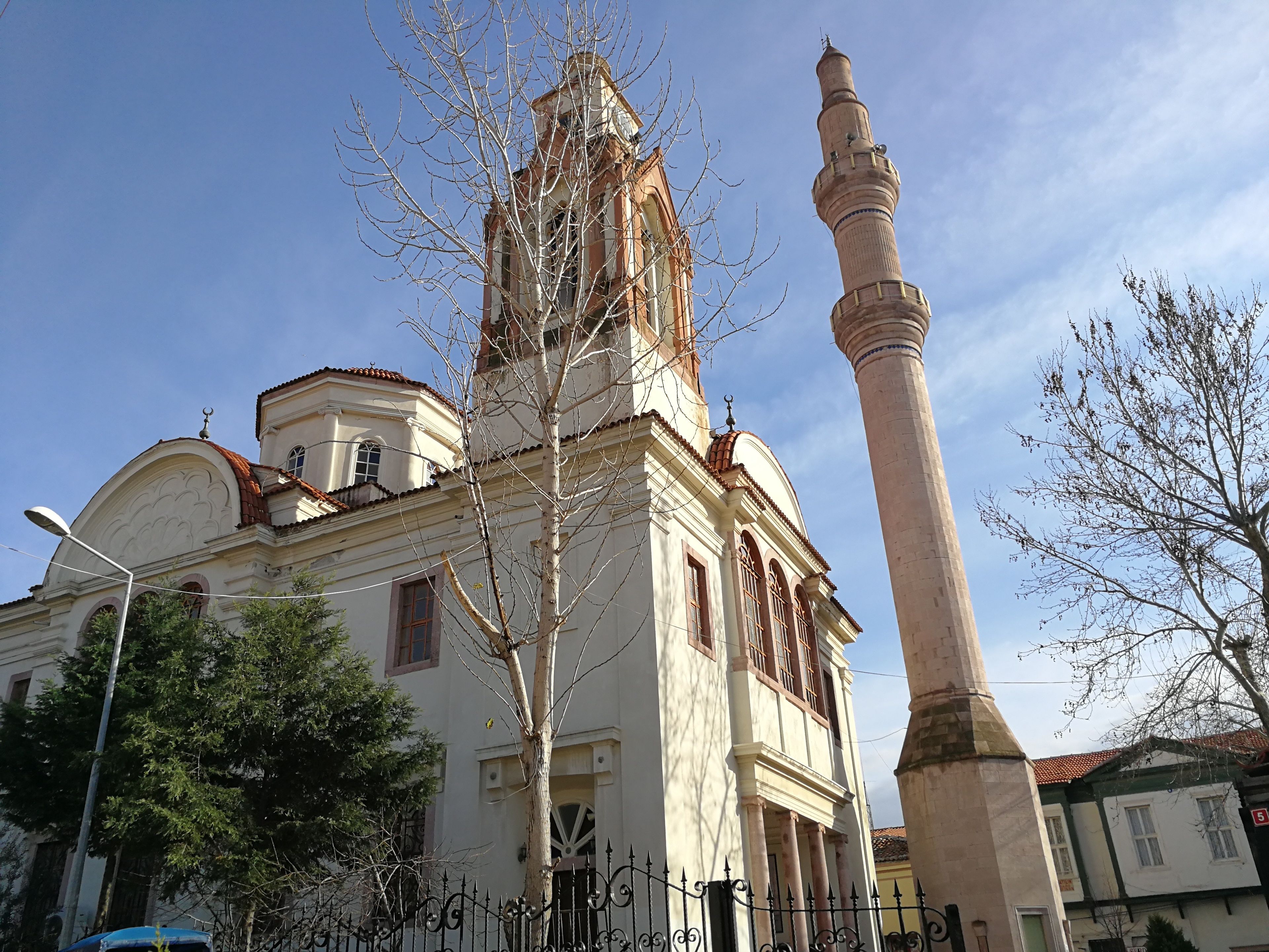 A historic building with a prominent tower and a tall minaret, surrounded by trees and a fence.