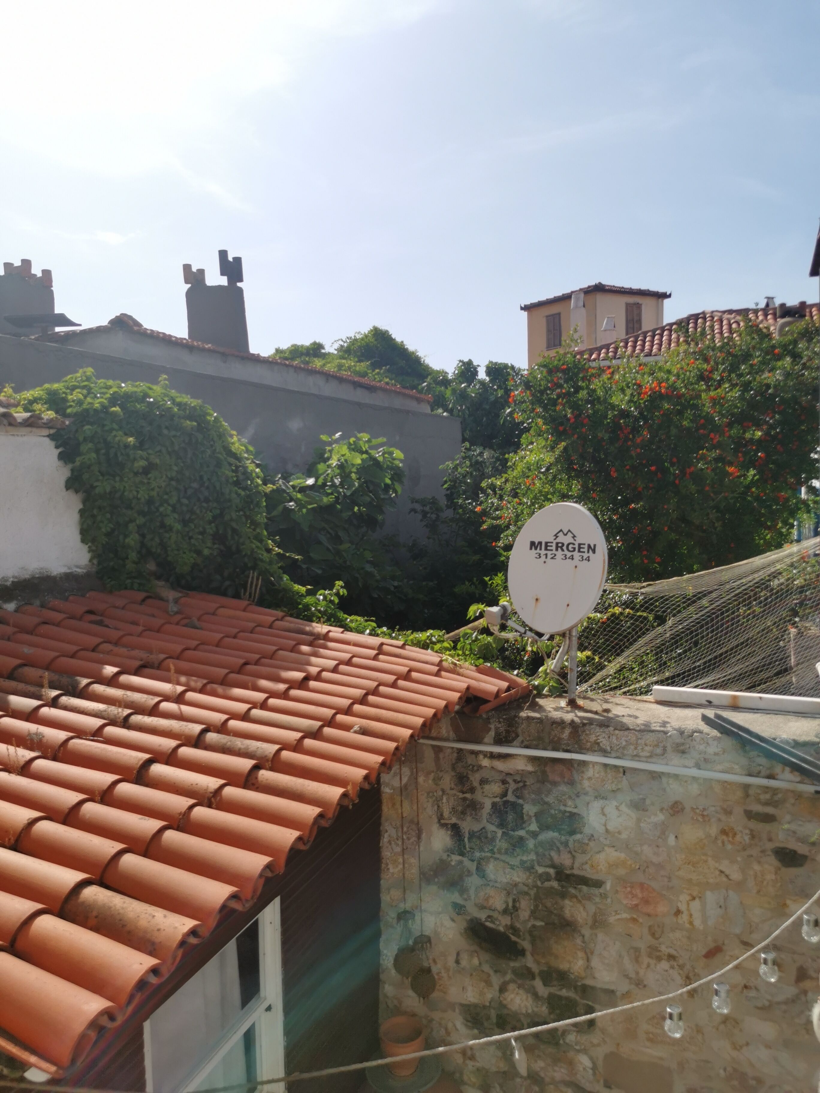 A rooftop with terracotta tiles, a satellite dish, and a stone wall.