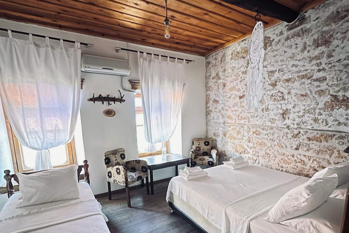 A rustic room with two beds, a stone wall, and a wooden ceiling.