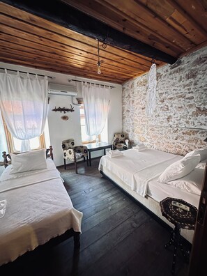 A rustic room with two beds, a stone wall, and a wooden ceiling. - Sahmeran Pansiyon (Ayvalik)