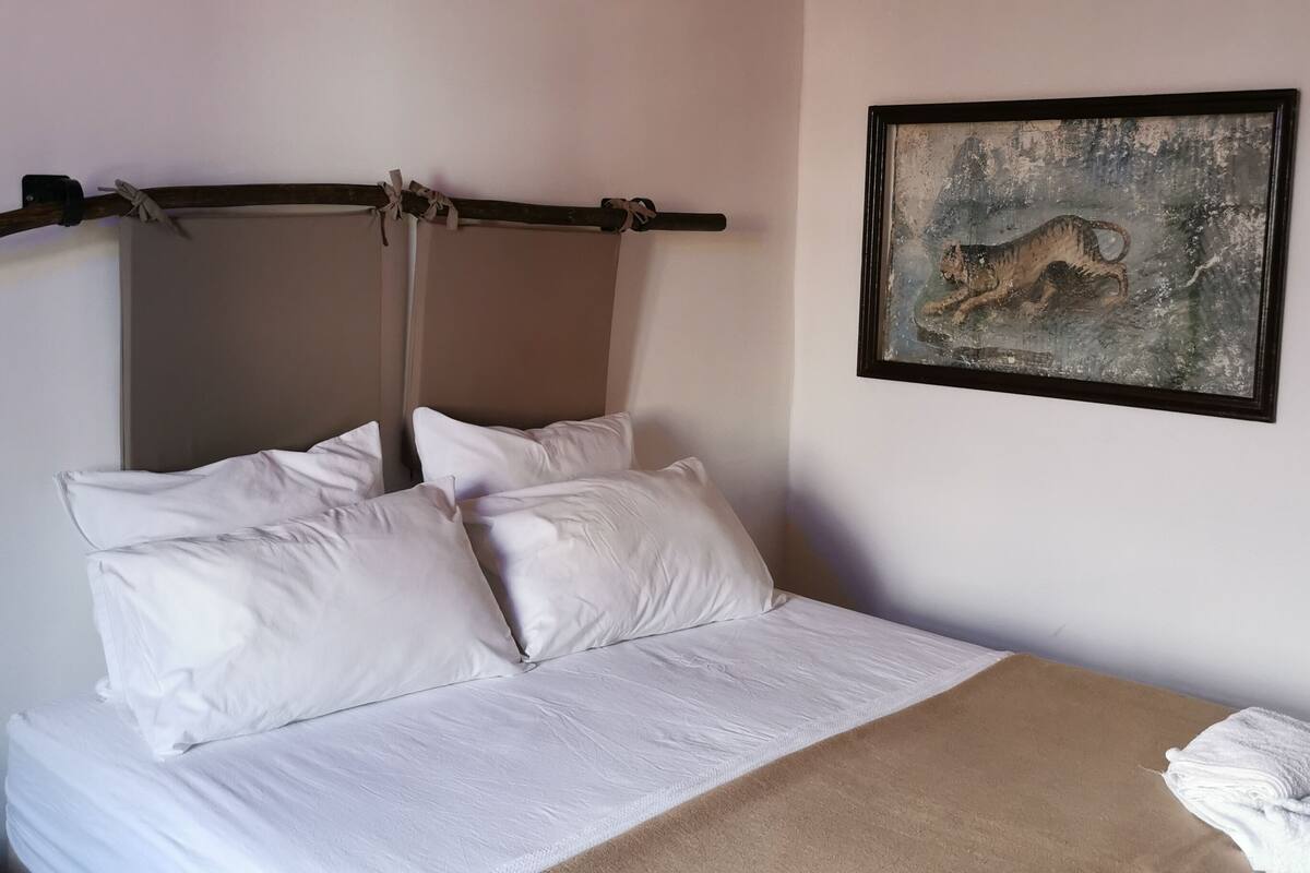 A neatly made bed with white linens and a beige blanket, a wooden headboard, and a framed painting of a tiger on the wall.