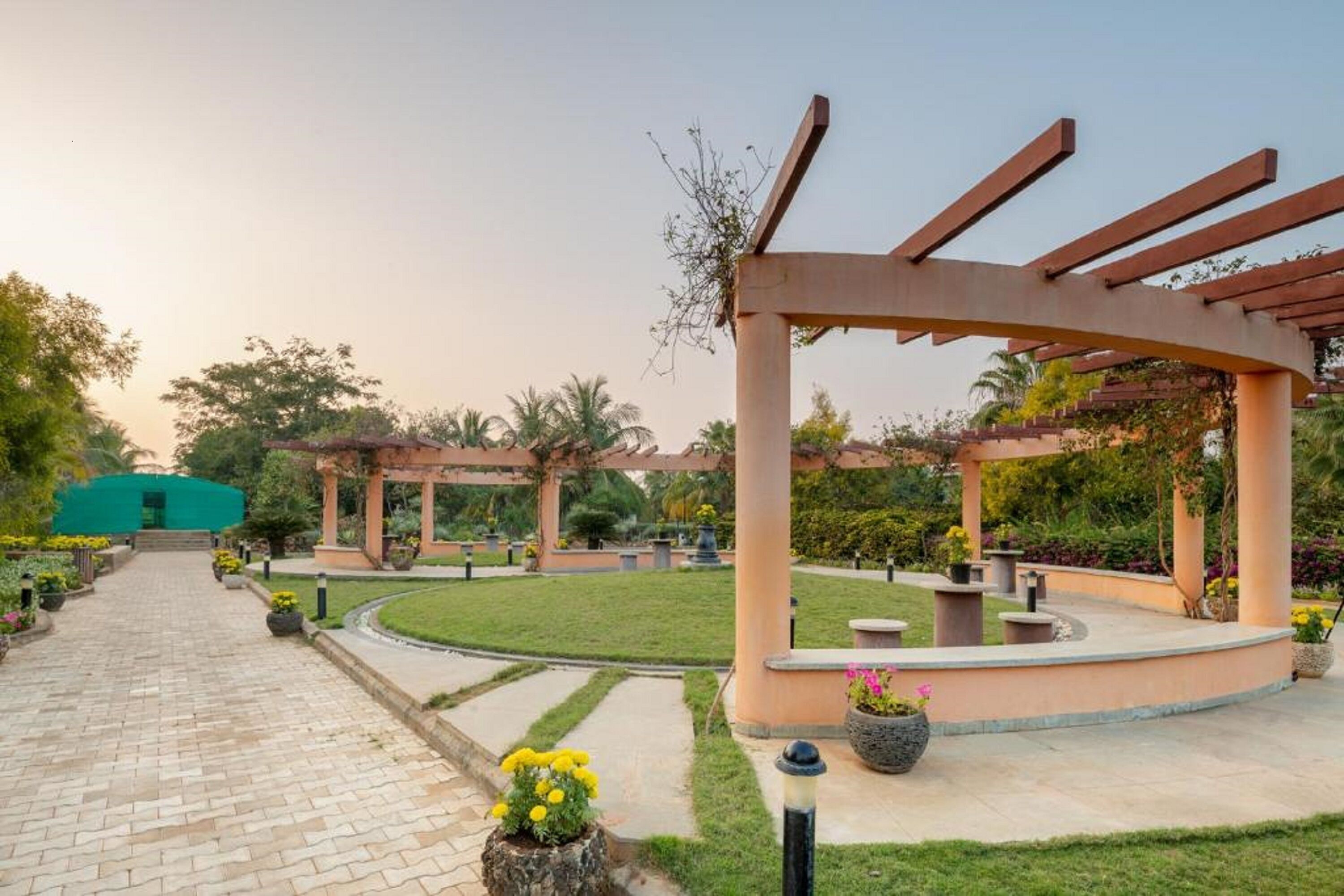 A garden pathway leading to a gazebo with a curved roof, surrounded by well-maintained grass and potted plants.