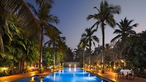 A swimming pool with palm trees on both sides, surrounded by tables and chairs. - Sunray Village Resort (Bhogopuram)