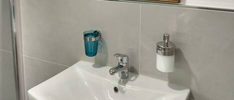 Un baño con un lavabo blanco, un espejo con marco dorado, un portavasos azul y un dispensador de jabón.