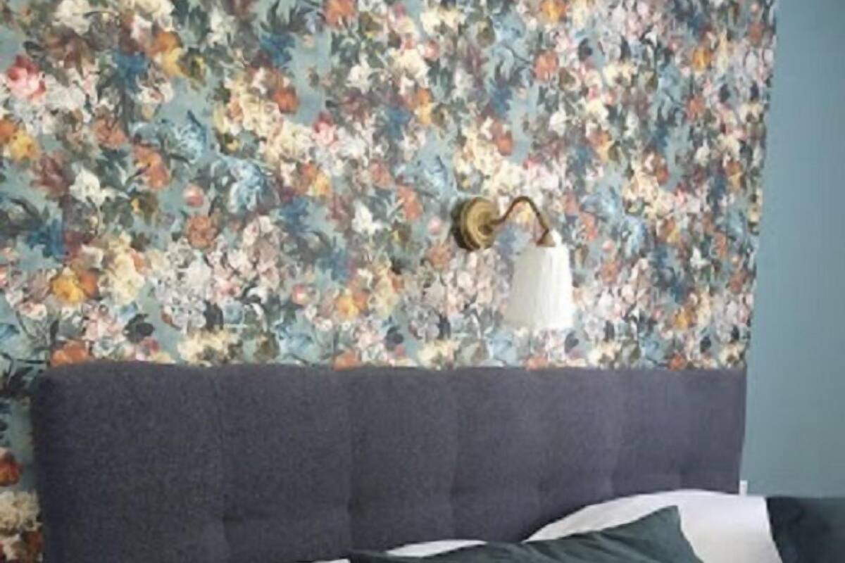A bed with white and dark green pillows, a grey headboard, and a floral wallpaper background.