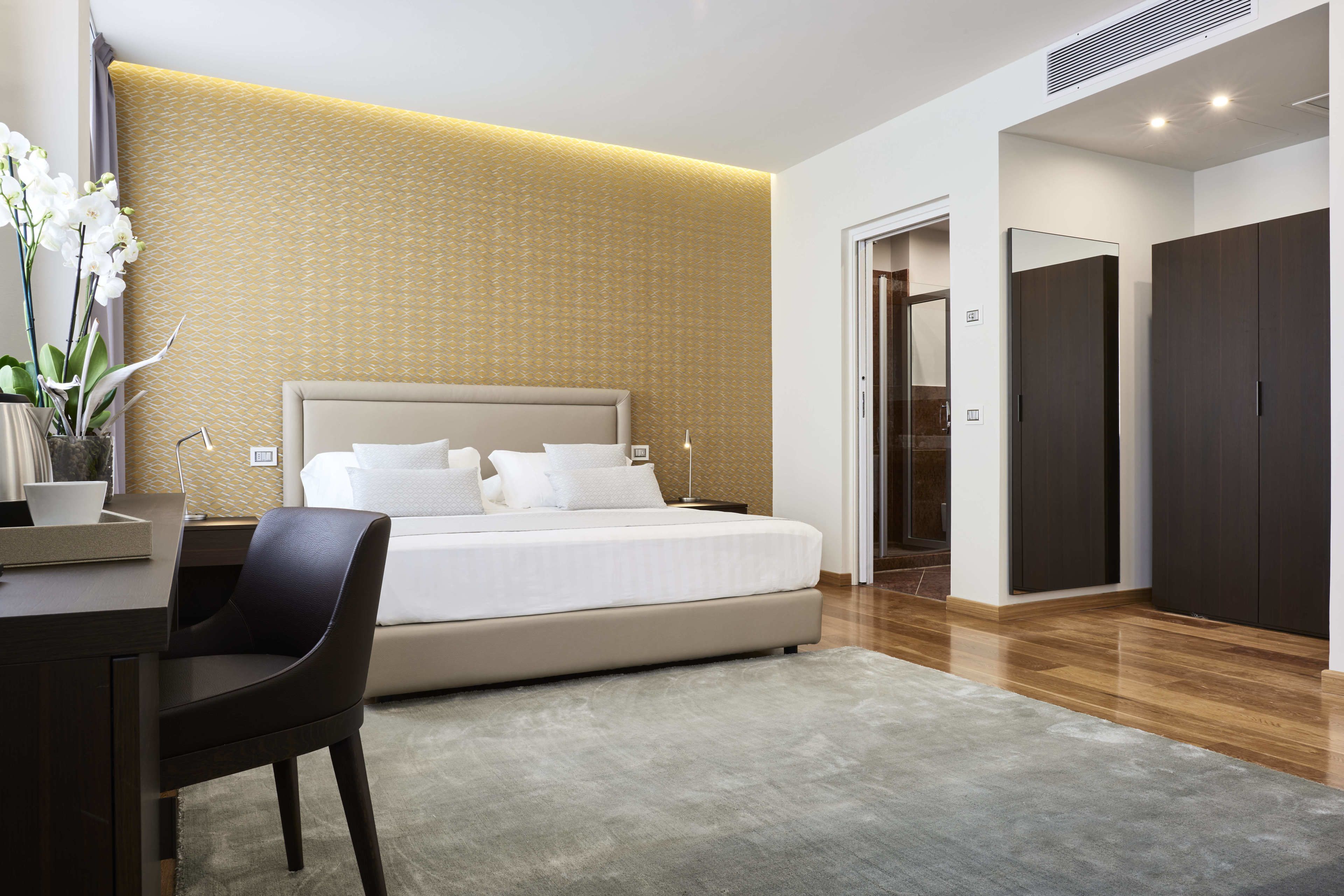 Een moderne hotelkamer met een groot bed, een bureau en een stoel. Er is een kledingkast en een deur die naar een andere kamer leidt.