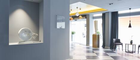 A hotel lobby with a checkered floor, a reception desk, and a wall-mounted sign indicating the location of the roof garden.
