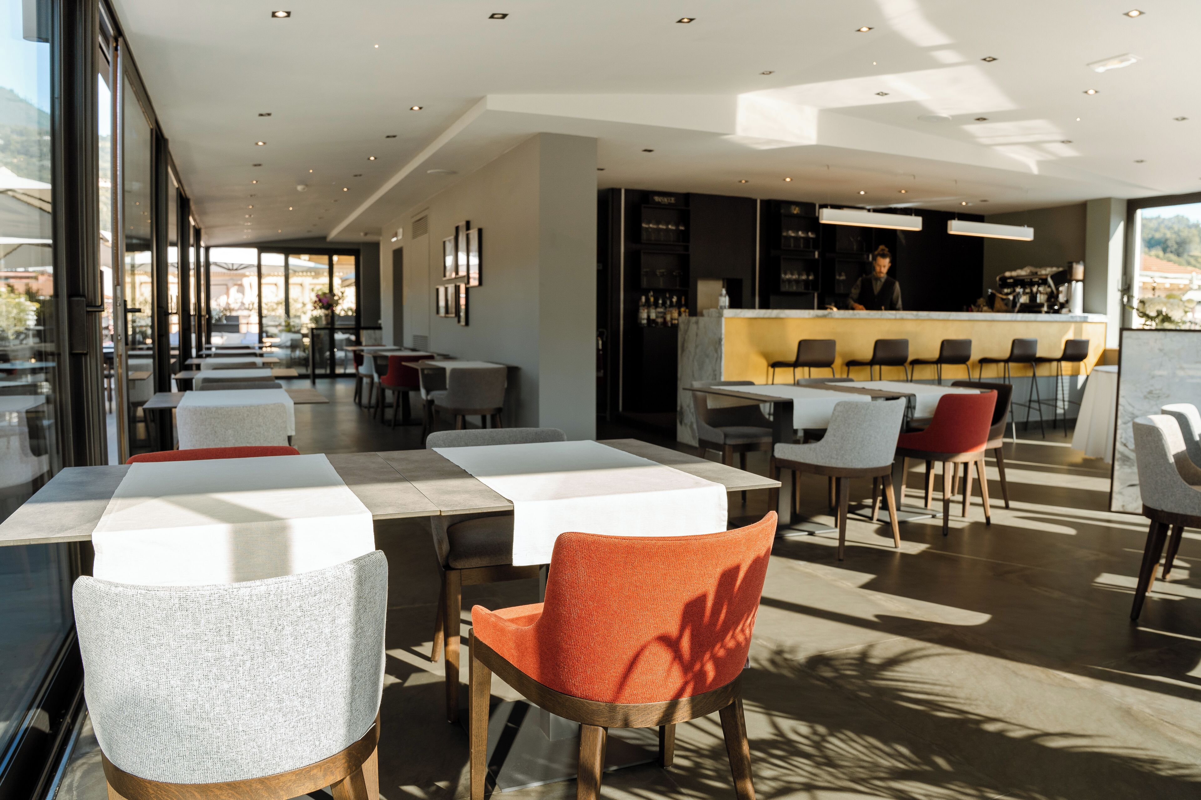 Restaurante moderno com área interna, bar e grandes janelas que oferecem vista para o exterior.