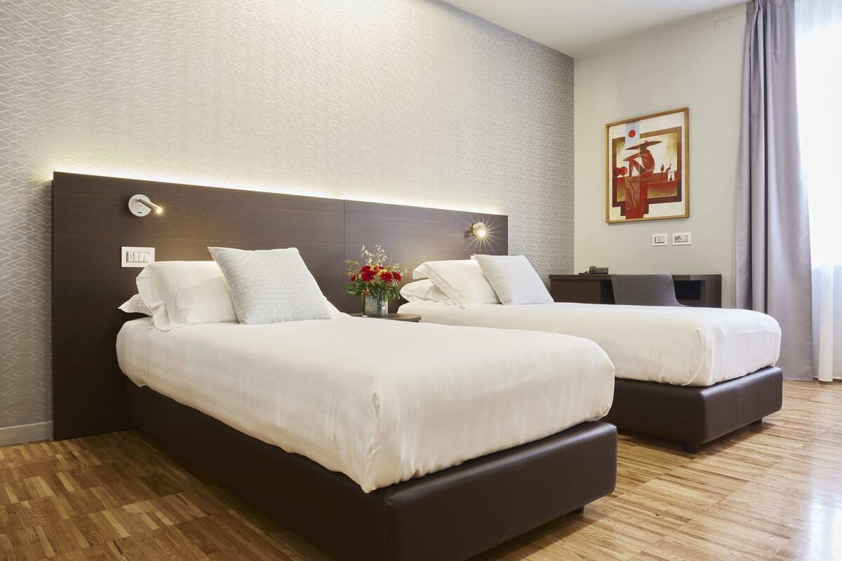 A hotel room with two beds, a modern headboard, a nightstand, and a painting on the wall.