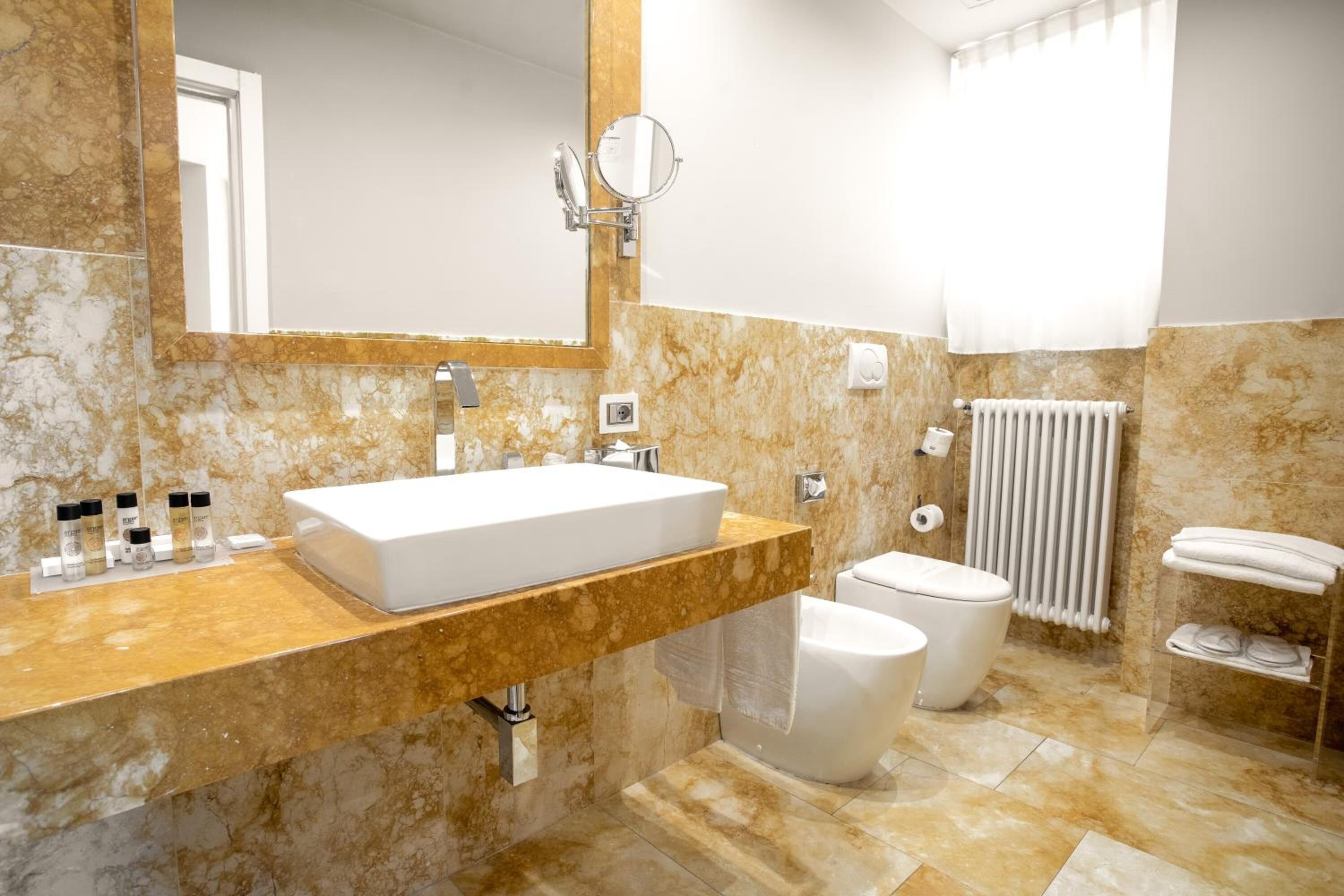 A modern bathroom with a marble vanity, a large mirror, a toilet, and a radiator.