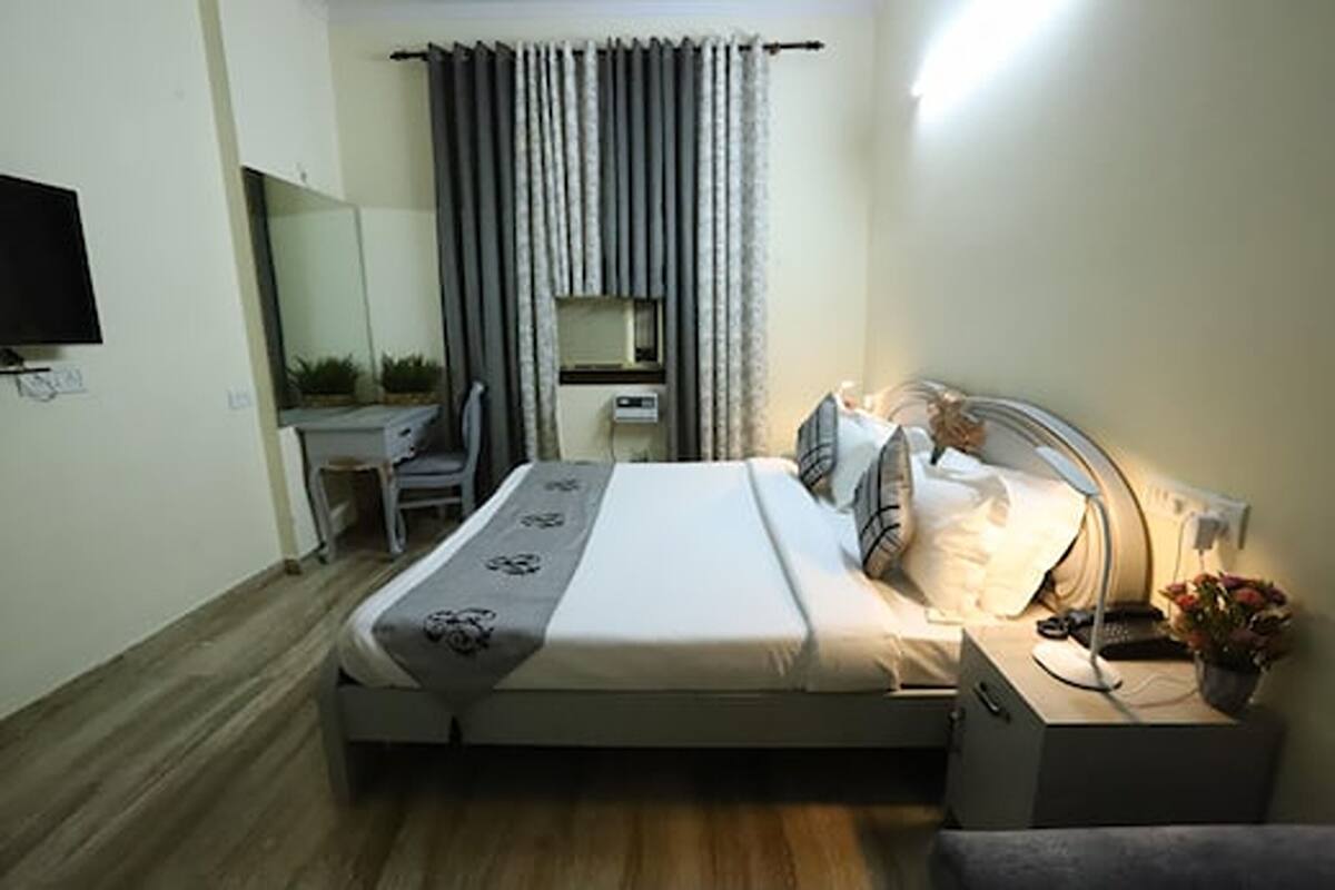 A bedroom with a bed, bedside table, lamp, and a small desk with a chair.