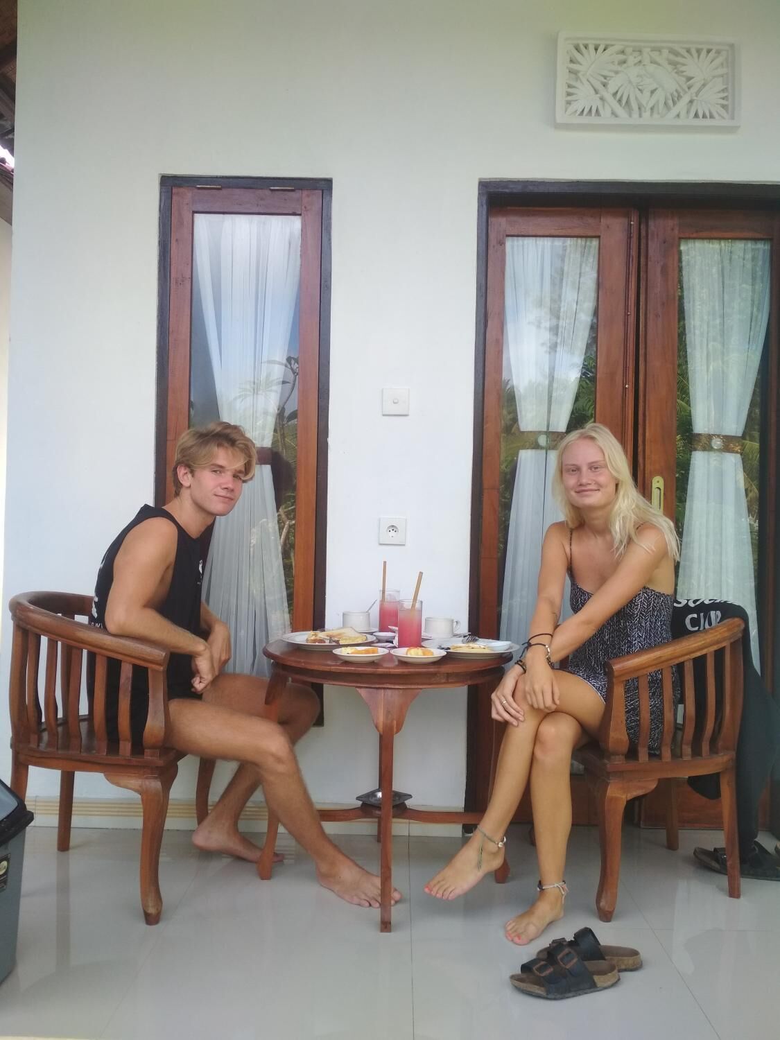 Dos personas sentadas en una mesa redonda de madera, con una pequeña bandeja de metal y un vaso de bebida roja.