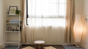 A room with a white round table, two beige cushions, a bookshelf with a plant, and a floor lamp. - Memory Traveler (Tainan)