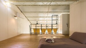 A spacious room with a wooden floor, a bed with a folded blanket, a ceiling fan, and a window with yellow curtains. - Memory Traveler (Tainan)
