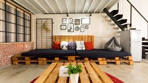 A modern living space with a wooden bench sofa, a small table with a plant, and a staircase. - Memory Traveler (Tainan)