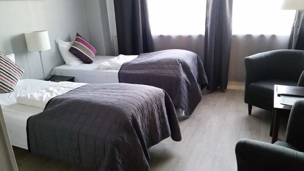 Una habitación de hotel con dos camas, un escritorio, una silla y una lámpara.