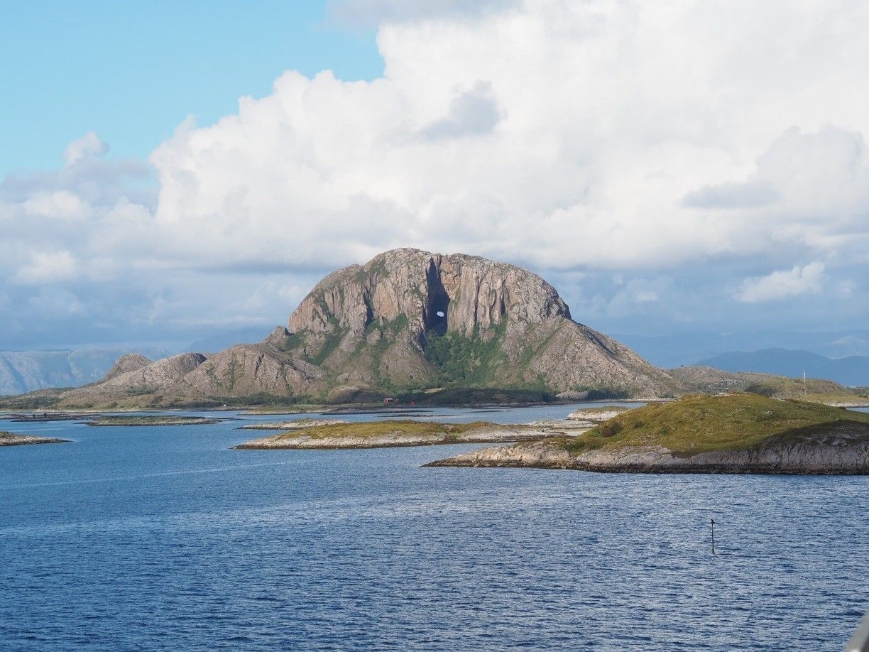 Een ruig, rotsachtig eiland met een grotachtige opening, omringd door kalm water en grasvelden.