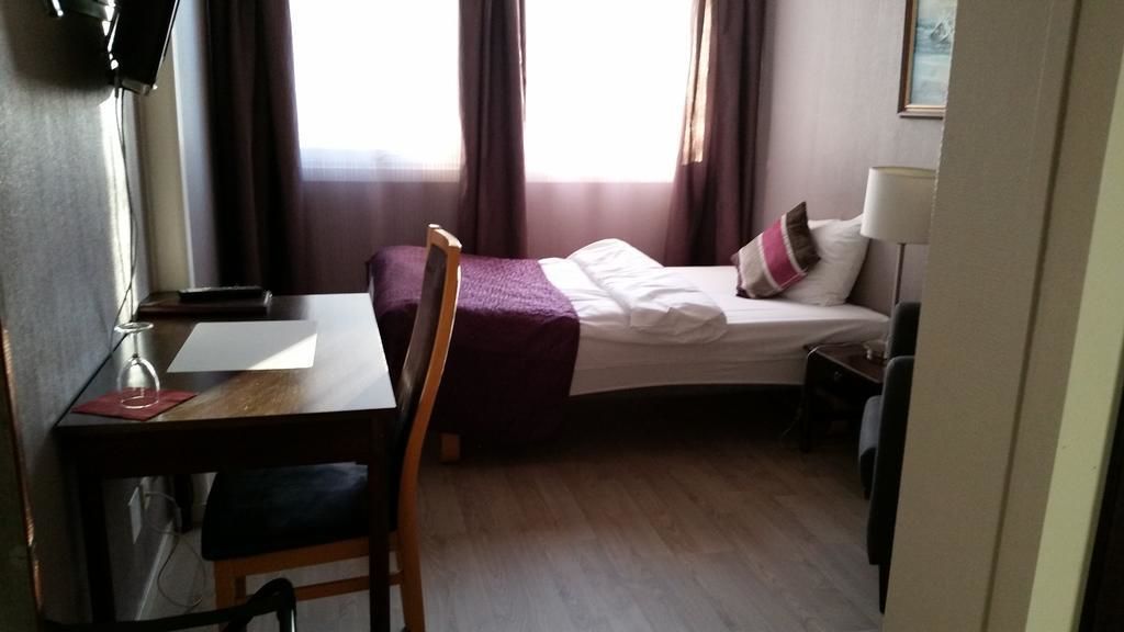 Een hotelkamer met een bed, een bureau, een stoel, een lamp en een raam met gordijnen.