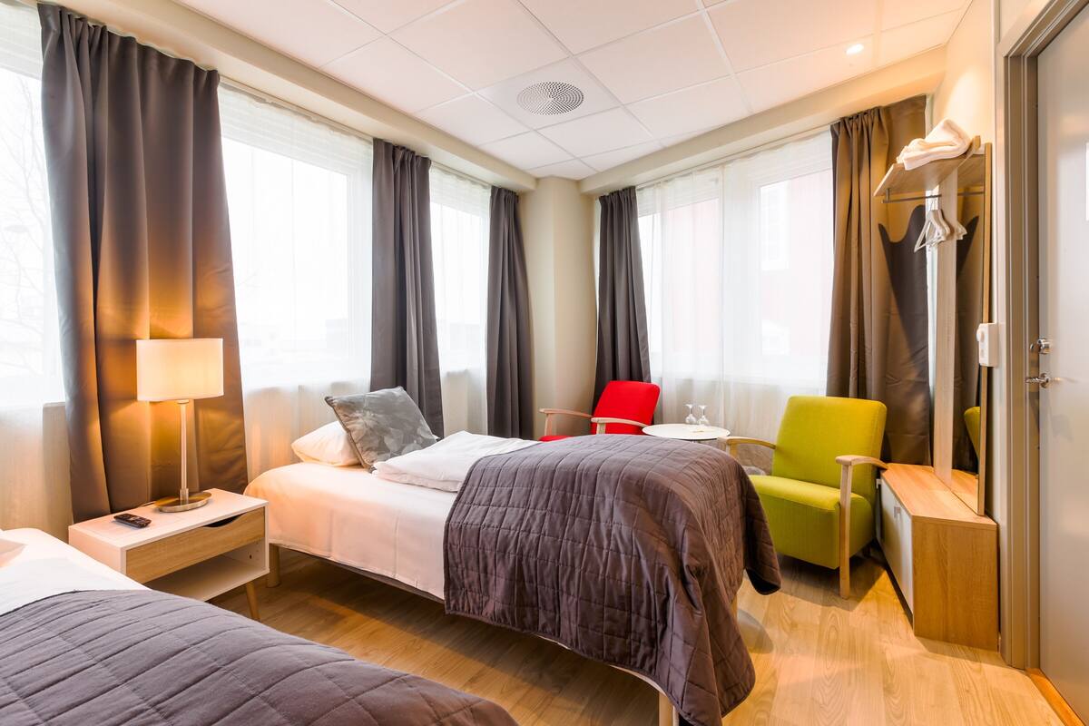 A hotel room with two beds, a desk, a chair, a lamp, and a wardrobe.