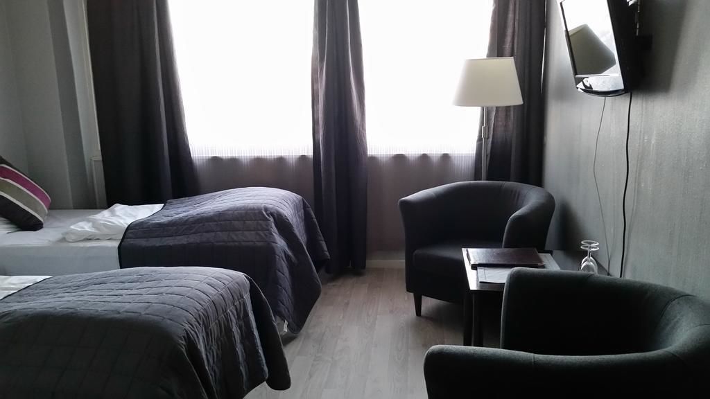 A hotel room with two beds, a desk, a chair, a lamp, and a TV.