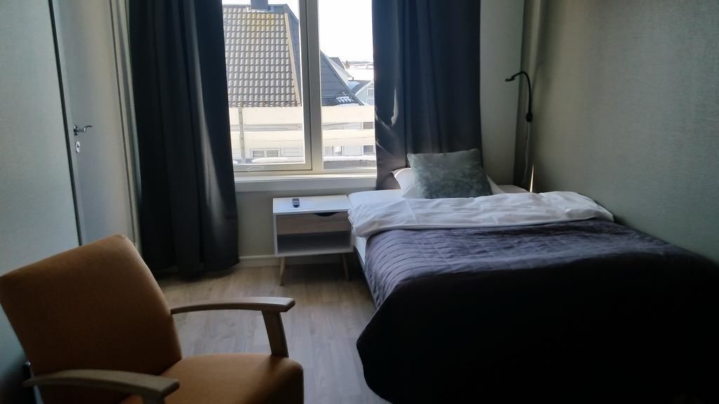 Una camera d'albergo con un letto, una sedia, un comodino e una finestra con tende.