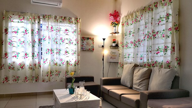 A living room with floral curtains, a sofa, a coffee table, and a wall-mounted shelf with decorative items.