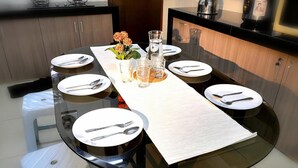 A dining table set for four with white plates, silverware, and a glass of water.