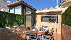Une terrasse avec une table dressée pour les repas, entourée de murs en pierre et une porte vitrée donnant sur un espace abrité.