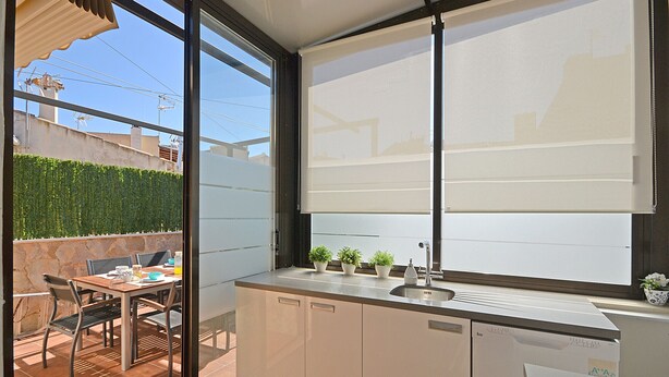 Une cuisine moderne dotée d’une grande fenêtre, un coin repas avec une table et des chaises, et un petit jardin visible à travers la fenêtre.