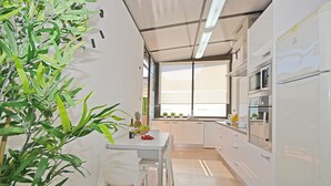 Une cuisine moderne avec des meubles blancs, une table à manger avec des chaises et une grande fenêtre qui laisse entrer la lumière naturelle.