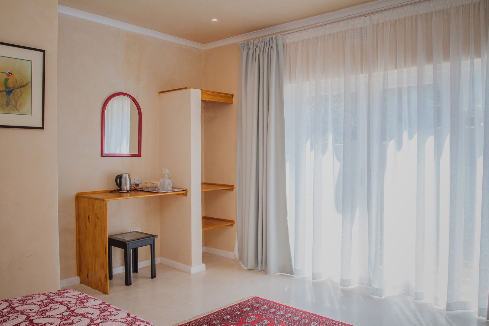 A room with a wooden desk, a chair, a mirror, and a window with sheer curtains.