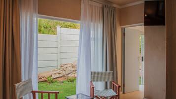 A room with a view of a garden, a door, and two chairs with a table.