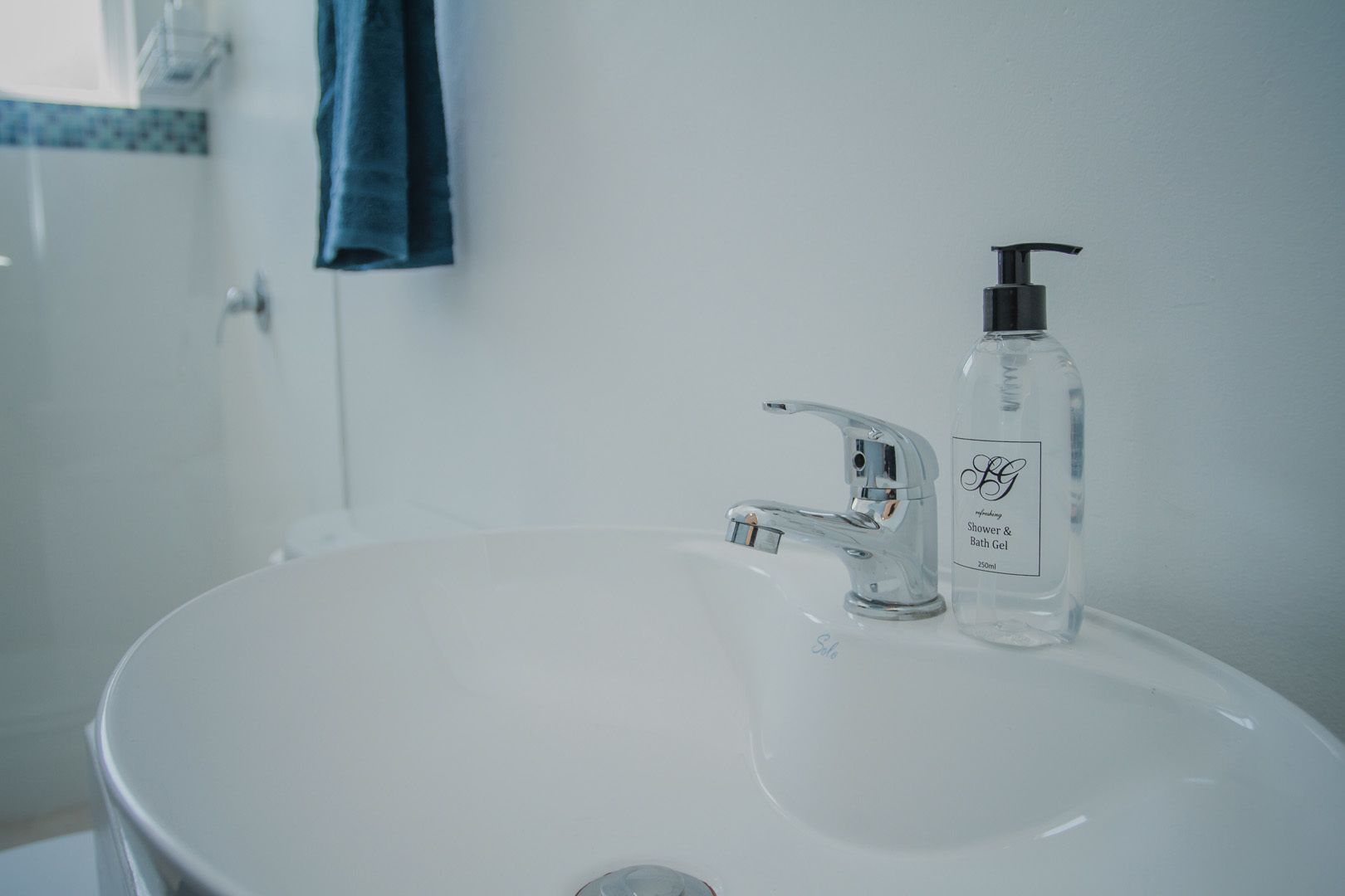 Un baño con un lavamanos blanco, un grifo moderno y una botella de gel de ducha y baño.