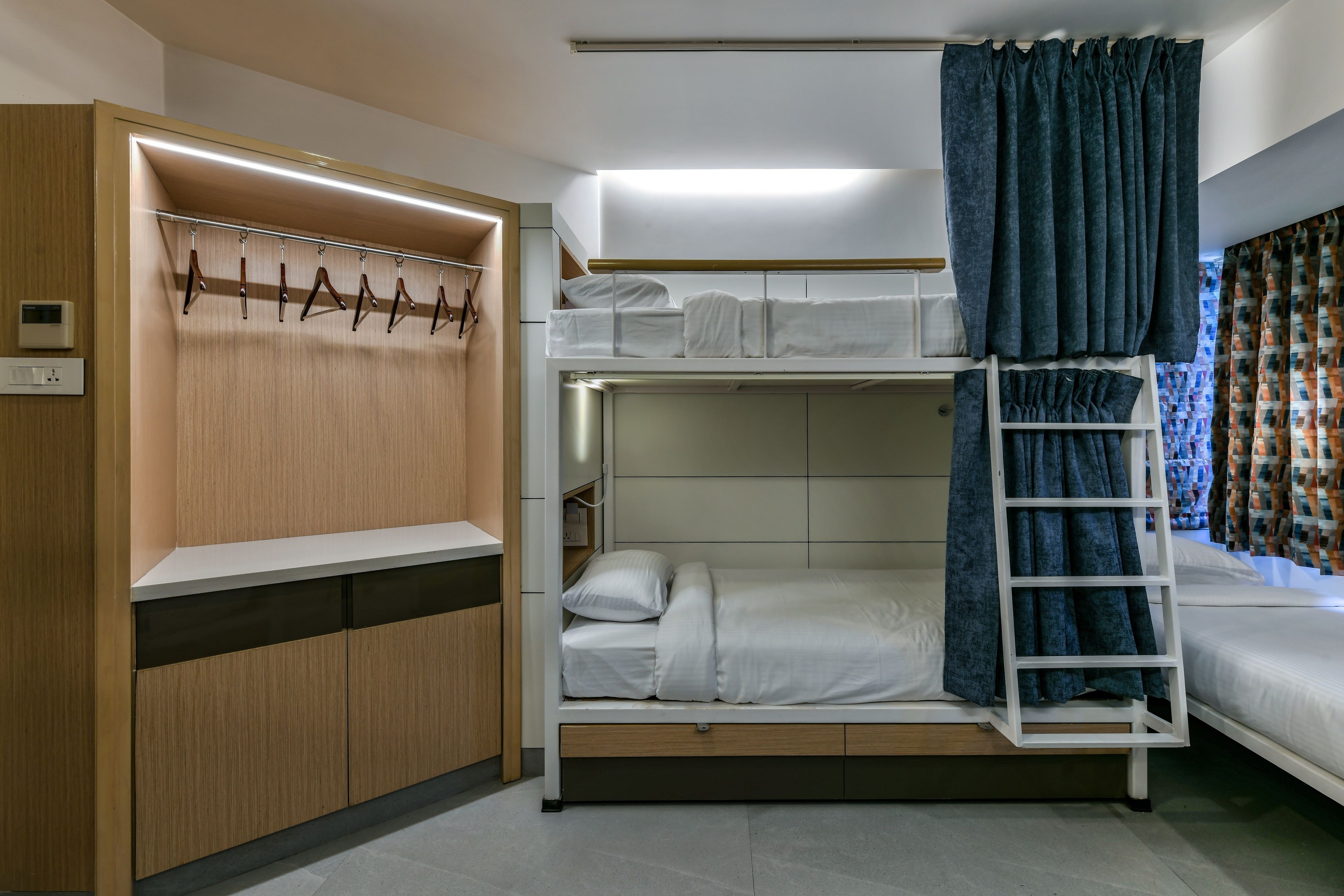 A bunk bed room with a wooden wardrobe, a ladder, and a curtain.