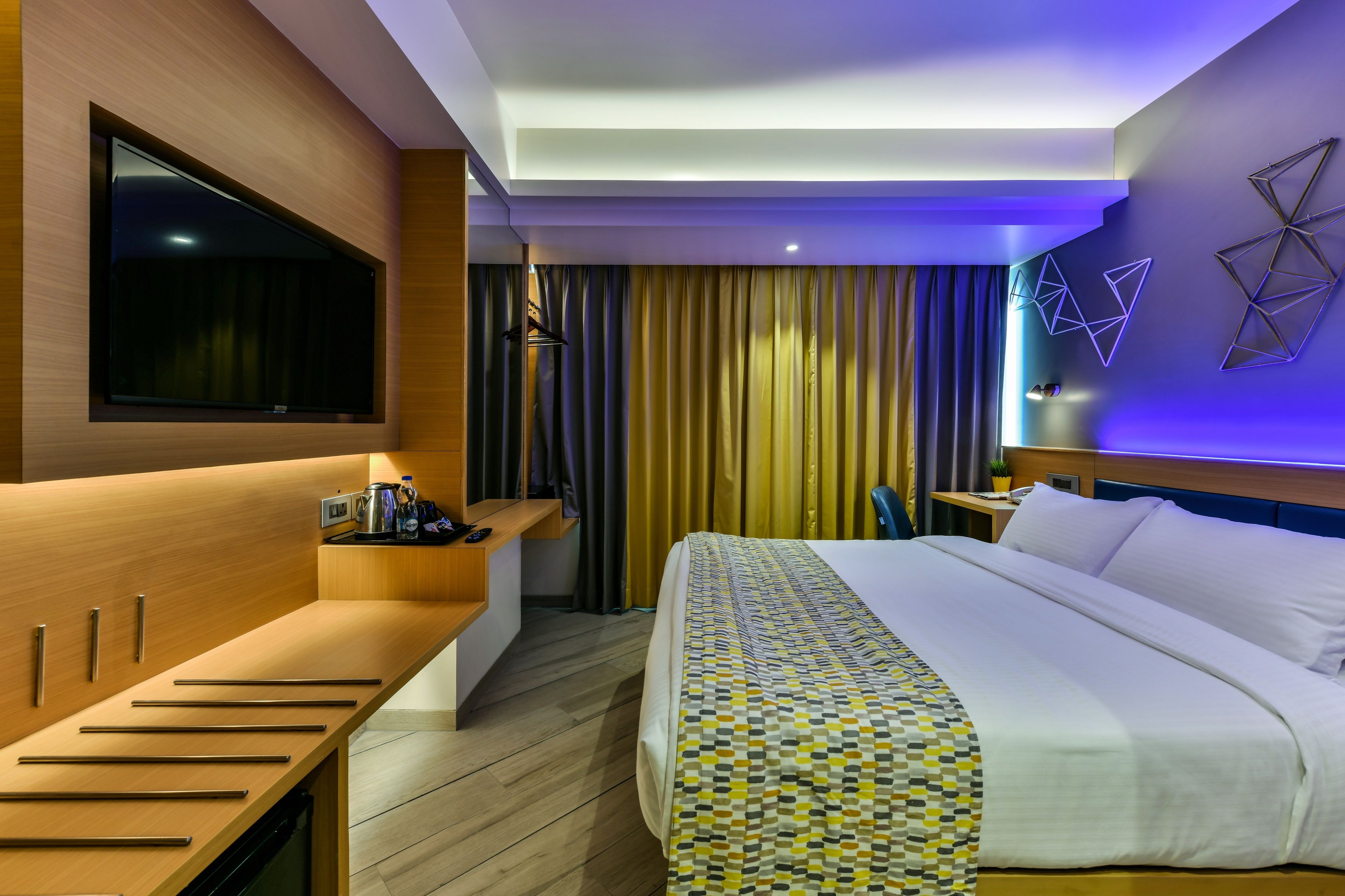 Habitación de hotel moderna con una cama grande, un televisor de pantalla plana montado en la pared, un escritorio de madera con una silla y una mesita de noche con una lámpara.