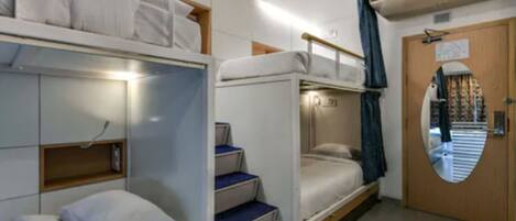 A compact, well-lit room with bunk beds, a small wardrobe, and a door with a mirror.