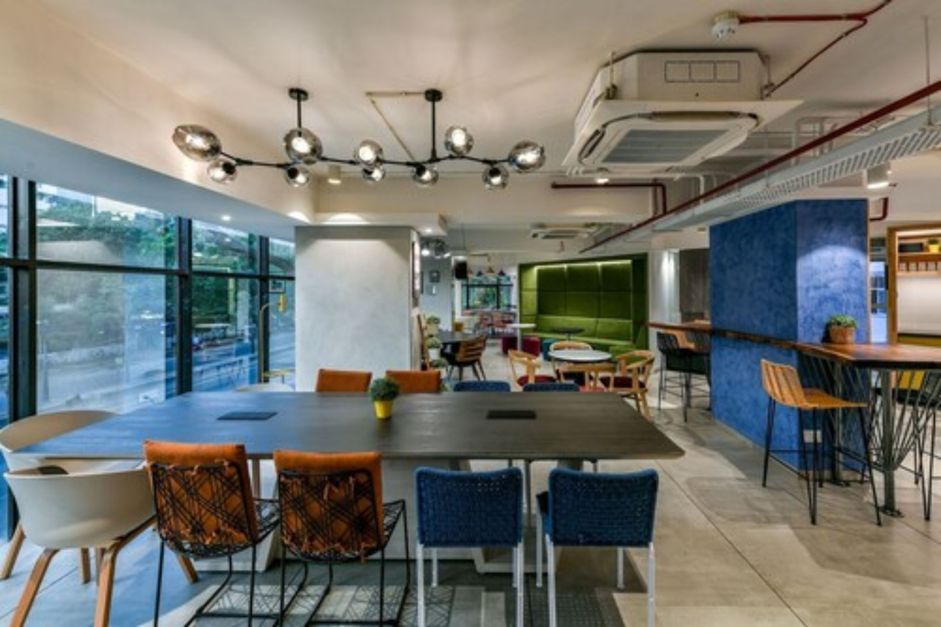 A modern dining area with a large table, blue chairs, and a green cushioned seating area.